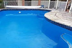  استخر شنا آبی رنگ با حاشیه سنگی در مقابل حصار سفید 